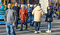 Fünf Personen bewegen sich über die Kirmes, lächelnd, sie unterhalten sich miteinander und mit einem an sie herantretenden jungen Paar.