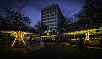 Das Rathaus im Dämmerlicht auf dem Platz davor zwei bunt beleuchtete Kinderkarussells