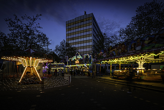 Das Rathaus im Dämmerlicht auf dem Platz davor zwei bunt beleuchtete Kinderkarussells