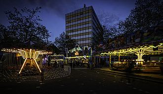 Das Rathaus im Dämmerlicht auf dem Platz davor zwei bunt beleuchtete Kinderkarussells
