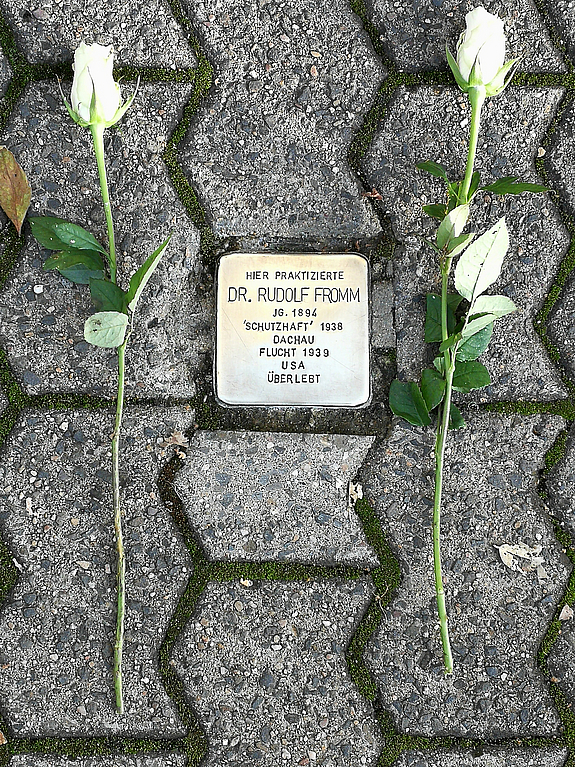 Ein Stolperstein neben dem zwei weiße Rosen zum Gedenken abgelegt wurden.
