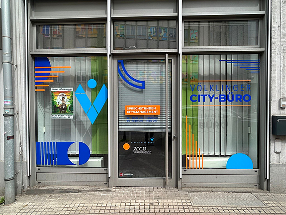 Eingang eines Ladenlokals mit mit Logos bunt beklebter Fenster-Front.