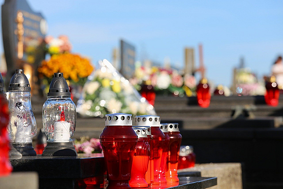 Mehrere Grablichter stehen auf einer Grabplatte auf einem Friedhof