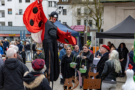 Ein als Marienkäfer verkleideter Stelzenläufer posiert vor Besucherinnen des Frühlingsmarktes