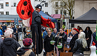 Ein als Marienkäfer verkleideter Stelzenläufer posiert vor Besucherinnen des Frühlingsmarktes
