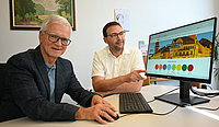 Oberbürgermeister und VHS-Direktor sitzen zusammen vor einem PC-Bildschirm auf dem die neue Webseite der VHS zu sehen ist.