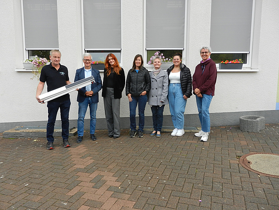 Beteiligte der Stadtverwaltung und der Geschäftsführer der ausführenden Firma stehen vor den Fenstern des Schulgebäudes an denen die Rollos zu sehen sind