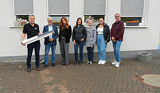 Beteiligte der Stadtverwaltung und der Geschäftsführer der ausführenden Firma stehen vor den Fenstern des Schulgebäudes an denen die Rollos zu sehen sind