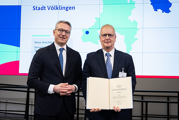 Minister und Projektleiter mit der Förderurkunde vor der Präsentationswand