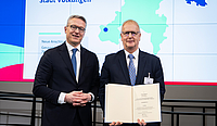 Minister und Projektleiter mit der Förderurkunde vor der Präsentationswand