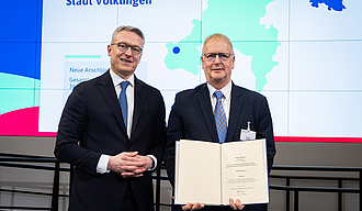 Minister und Projektleiter mit der Förderurkunde vor der Präsentationswand