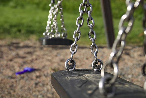 Schwarzer Schaukelsitz an Kette auf Spielplatz im Hintergrund Wiese