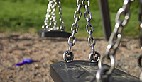 Schwarzer Schaukelsitz an Kette auf Spielplatz im Hintergrund Wiese