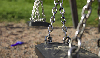 Schwarzer Schaukelsitz an Kette auf Spielplatz im Hintergrund Wiese