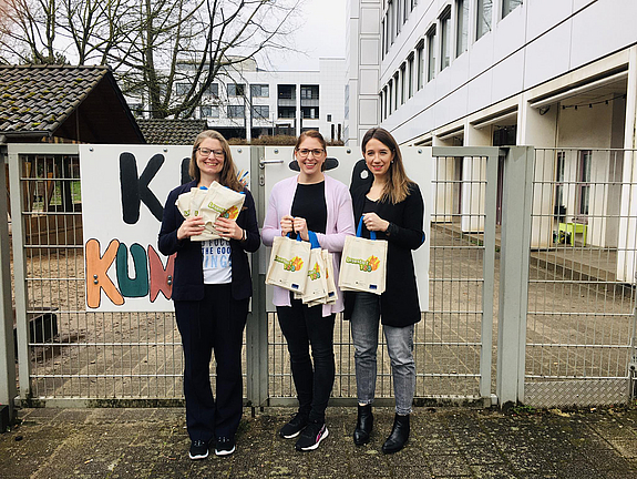 Drei Frauen stehen vor dem Eingan zu einer Kita und halten die Lesestart-Tüten in den Händen